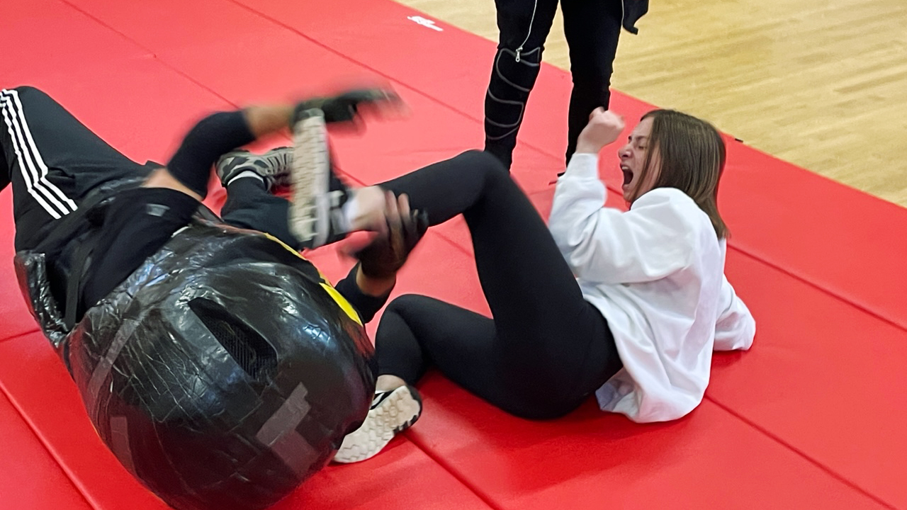 ESD student fighting an instructor dressed as an assailant on  a mat in class.